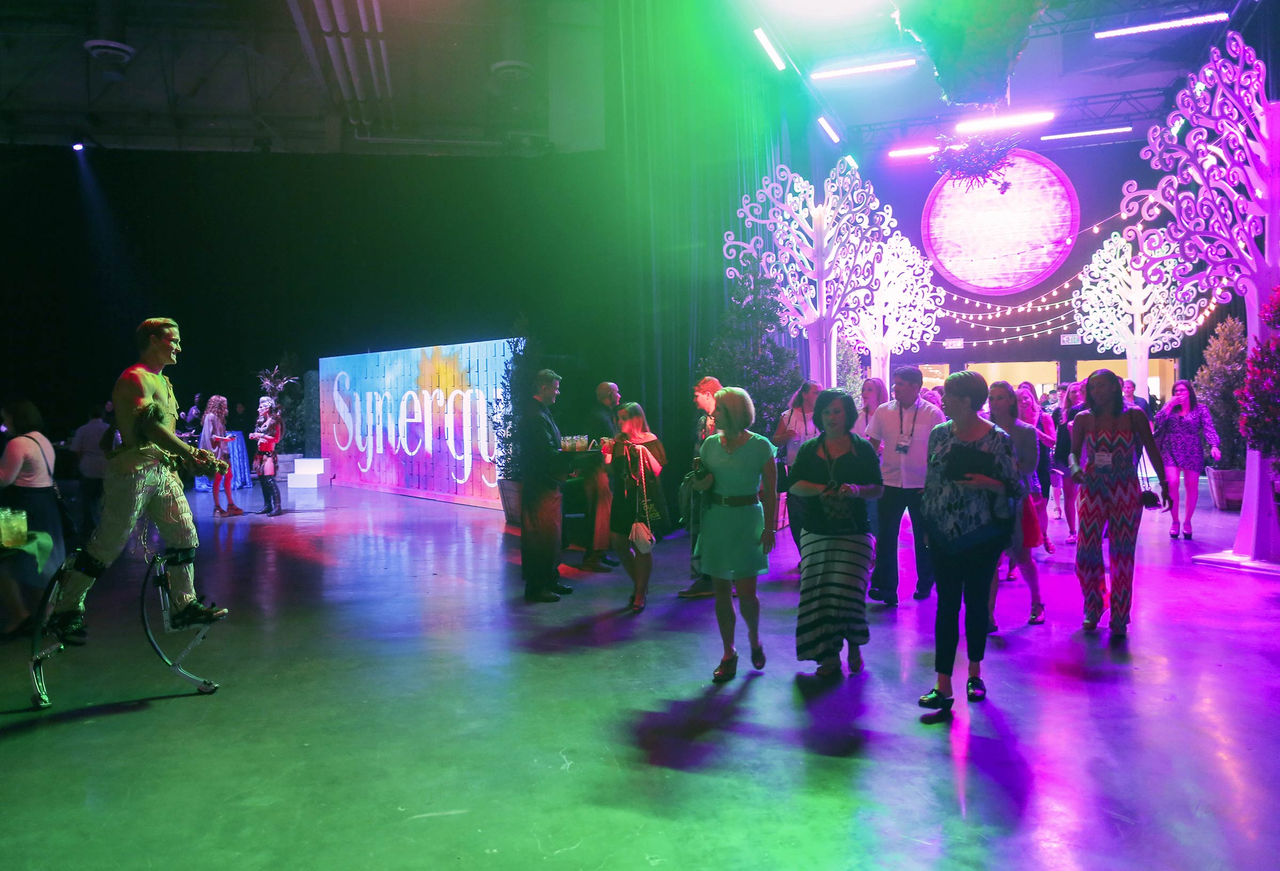 Interior of expo hall c during an event, with green and purple lights and people mingling.