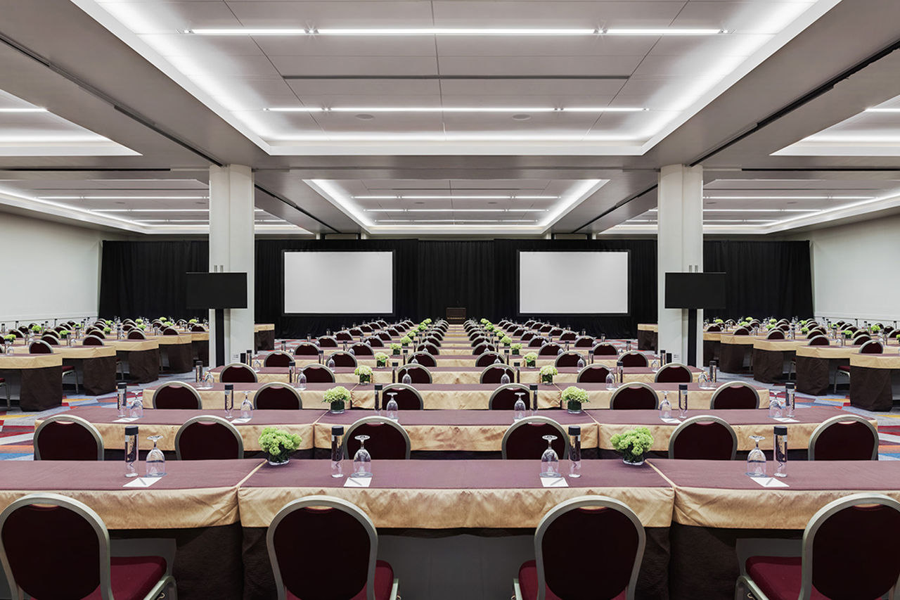 A room setup for an event with rows of tables and 2 projector screens on the wall. 